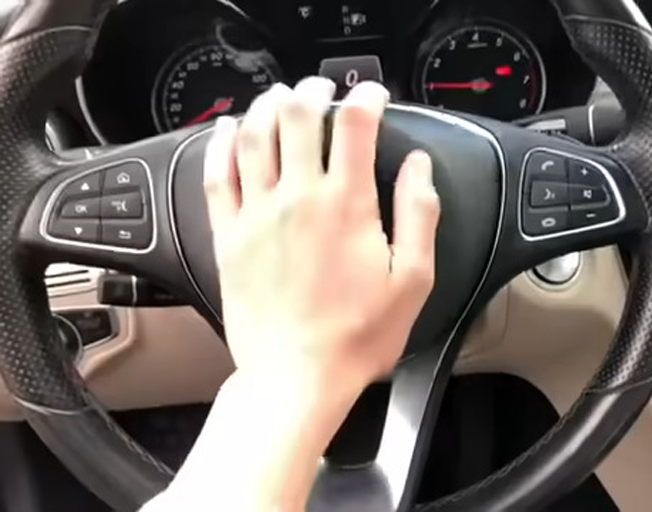 A hand on the horn pad on a car steering wheel