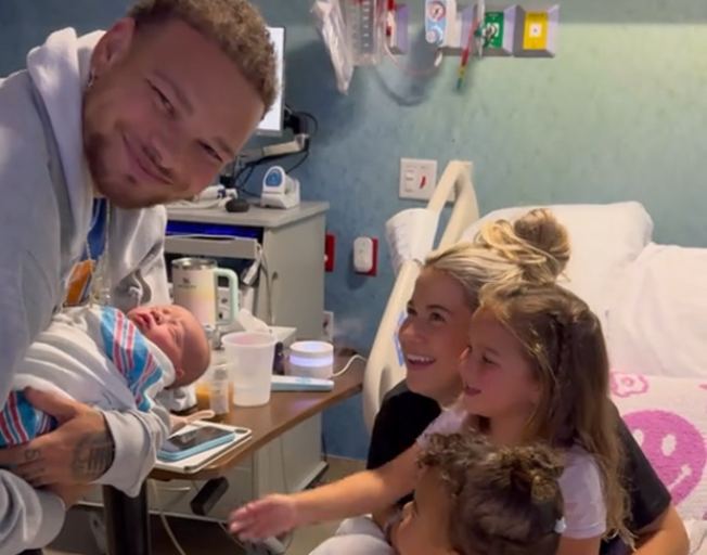 Kane Brown holding Krewe Allen with Katelyn Brown, Kingsley Rose and Kodi Jane sitting on a hospital bed 6-8-24