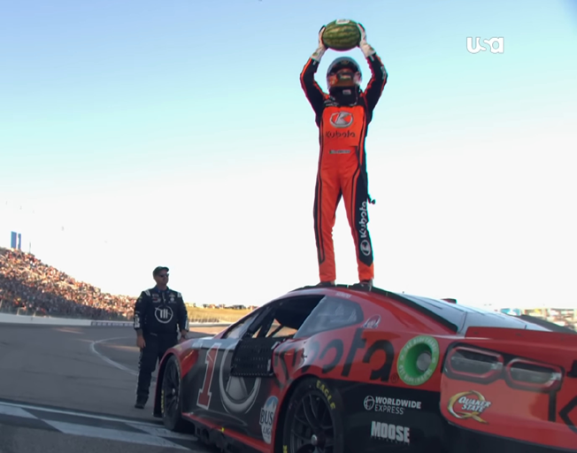 Ross Chastain holding a watermelon standing on his racecar's roof at Kansas Speedway 9-29-24